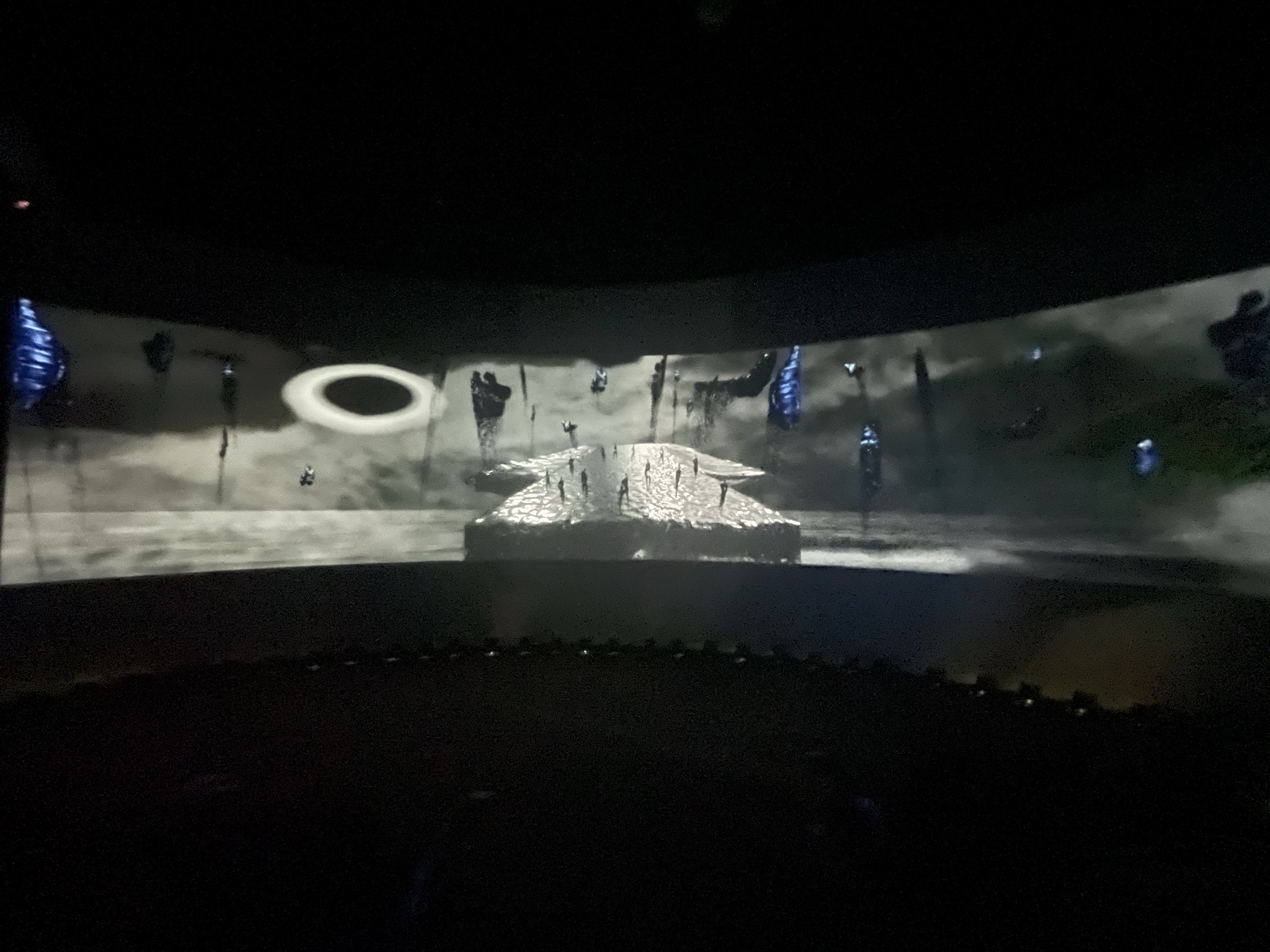 Curved panoramic screen showing figures on a platform